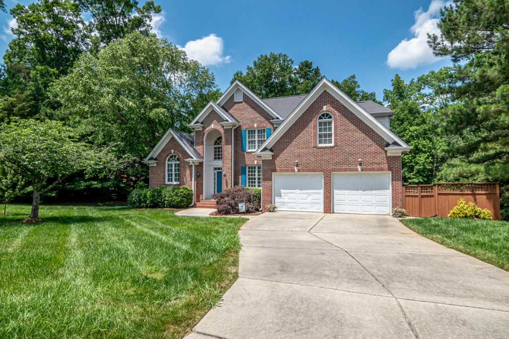 Brick two-story house with three-car garage, arched windows, blue shutters, and a manicured lawn.